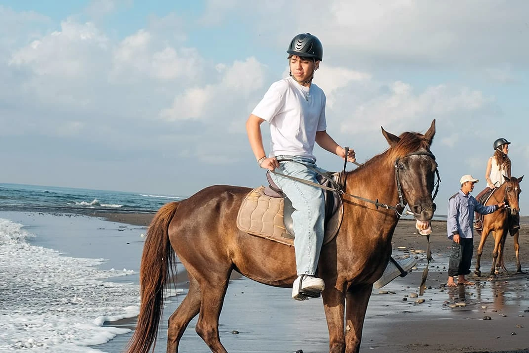 young boy riding a strong horse guided by a professional